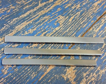 Puede incluir: Tres tiras de metal plateado, dispuestas horizontalmente sobre una superficie de madera azul y marrón.