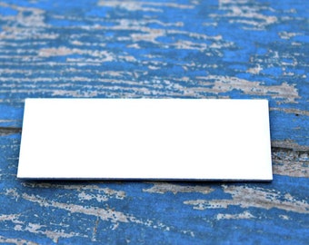 Op de afbeelding: Een blanco wit rechthoekig kaartje op een blauw houten oppervlak met een verweerde afwerking.