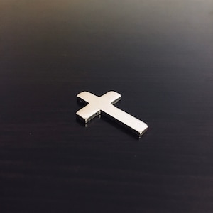 May include: A silver cross on a dark wood surface.