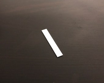 May include: A white rectangular piece of paper on a dark brown surface.