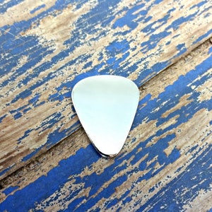 May include: A silver guitar pick on a blue and brown wooden surface.
