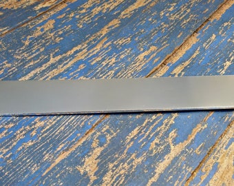 Può includere: Una lunga e sottile barra di metallo argentata con bordi arrotondati. La barra è appoggiata su una superficie di legno blu e marrone.