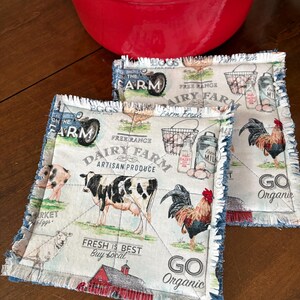 May include: Two farm-themed quilted pot holders with a red pot in the background. The pot holders feature images of farm animals, eggs, and text that reads "Dairy Farm Artisan Produce", "Fresh is Best Buy Local", and "Go Organic".