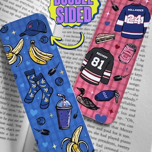 Op de afbeelding: Dubbelzijdige boekenlegger met blauwe en roze ontwerpen. De blauwe kant heeft bananen, bosbessen, sokken, een hoed en een smoothie. De roze kant heeft hockeytruien, een sandwich en ginger ale.