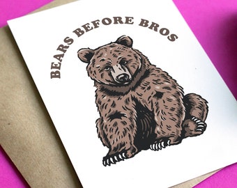 May include: Greeting card with a brown bear illustration and the text "BEARS BEFORE BROS" in brown. The card is on a kraft paper envelope, with a purple flower on a bright pink background.
