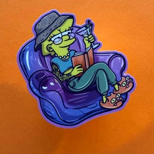 May include: A sticker featuring a cartoon character with yellow skin, wearing glasses, a hat, and a blue shirt, seated in a purple chair. The character holds a martini and a book. The sticker has a purple outline and is set against an orange background.