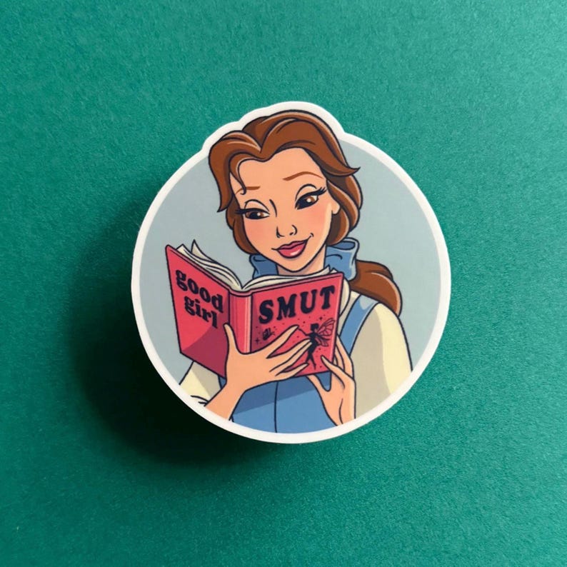 May include: A sticker featuring a cartoon illustration of Belle from Beauty and the Beast reading a book titled "good girl SMUT".