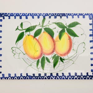 May include: A rectangular ceramic tile featuring a hand-painted illustration of three yellow and orange lemons with green leaves and thin, swirling vine accents. The tile is framed by a decorative blue and white geometric border pattern.