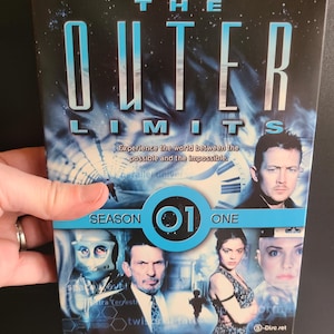May include: DVD box set for "The Outer Limits" Season 1. The cover features a blue and black background with the show's title in large, stylized letters. Images of actors and a clock are also visible.