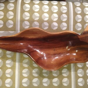 May include: A large, wooden serving bowl carved in the shape of a leaf. The bowl is made of dark brown wood and has a smooth, polished finish.