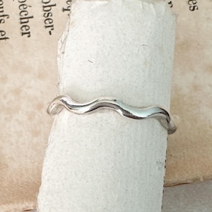 May include: A silver ring with a wavy design. The ring is made of a smooth, polished metal.
