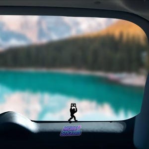 May include: A black silhouette of a person holding a boombox, with the text "MORE STICKERS" below. The image is set against a blurry background of a lake and mountains.