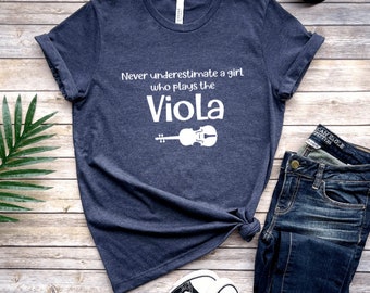 May include: A dark blue t-shirt with white text that reads "Never underestimate a girl who plays the Viola" and a white outline of a viola.