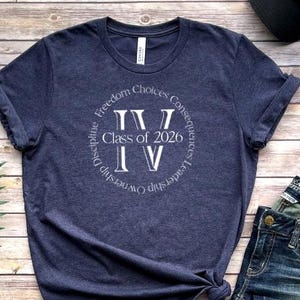 May include: A dark blue t-shirt with a white circle graphic that says "Class of 2026" and has the Roman numeral "IV" inside the circle. The circle also has the words "Freedom Choices Consequences Leadership Ownership Discipline" around the outside.