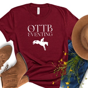May include: Burgundy t-shirt with white text that reads "OTTB Eventing" and a silhouette of a rider jumping a horse.