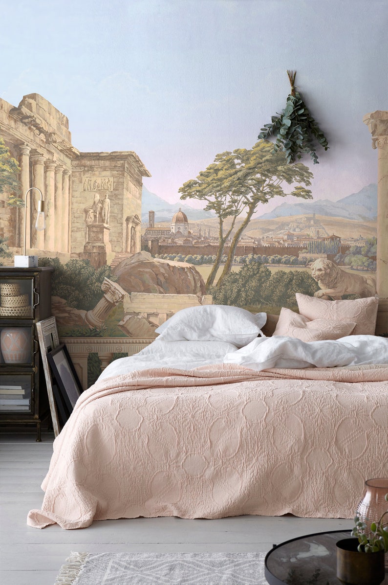 Op de afbeelding: Een roze gestikte bedsprei met witte linnen kussens op een bed voor een muurschildering die een oude Romeinse stad voorstelt.