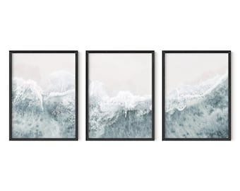Può includere: Un set di tre stampe incorniciate che mostrano una vista aerea di onde oceaniche che si infrangono su una spiaggia di sabbia. Le onde sono di colore blu chiaro e bianco, e la sabbia è di colore beige chiaro.