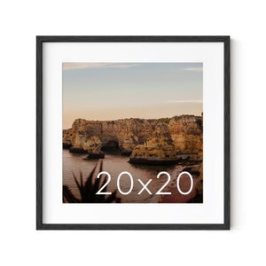 May include: A framed photograph of a rocky coastline with a blue sky and ocean. The image is in a black frame and has the text "20x20" printed on it.