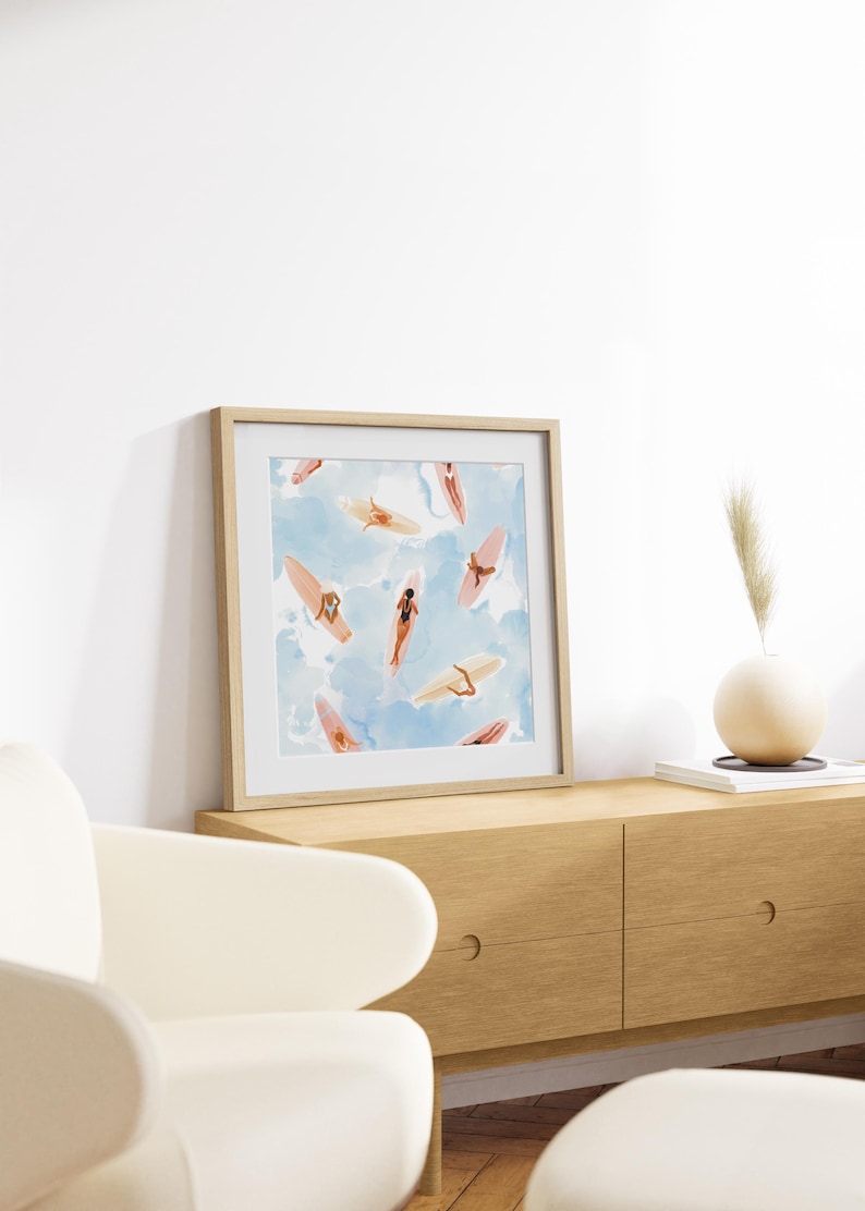 May include: A framed print of a watercolor painting depicting a pattern of women on surfboards against a blue and white background.