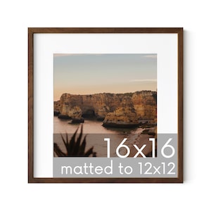 May include: A brown wood picture frame with a matted opening. The frame is 16x16 inches and the matted opening is 12x12 inches. The image inside the frame is a landscape photograph of a rocky coastline at sunset.