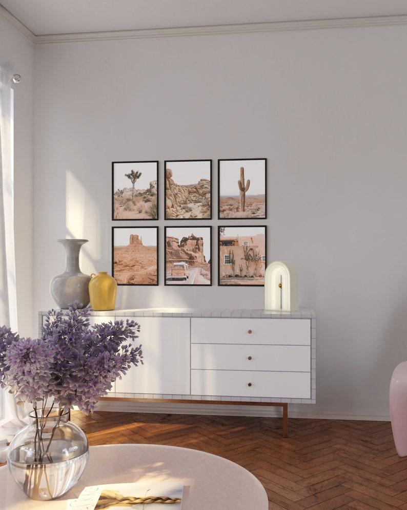 Pu&ograve; includere: Una cassettiera bianca con tre cassetti e pomelli dorati si trova in un soggiorno con un pavimento in legno chiaro. Una lampada bianca con un arco dorato si trova sopra la cassettiera. Sei stampe incorniciate di paesaggi desertici sono appese al muro sopra la cassettiera.