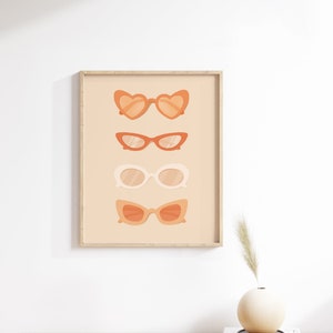 May include: A framed print with a peach background featuring four different styles of sunglasses in shades of orange and white.