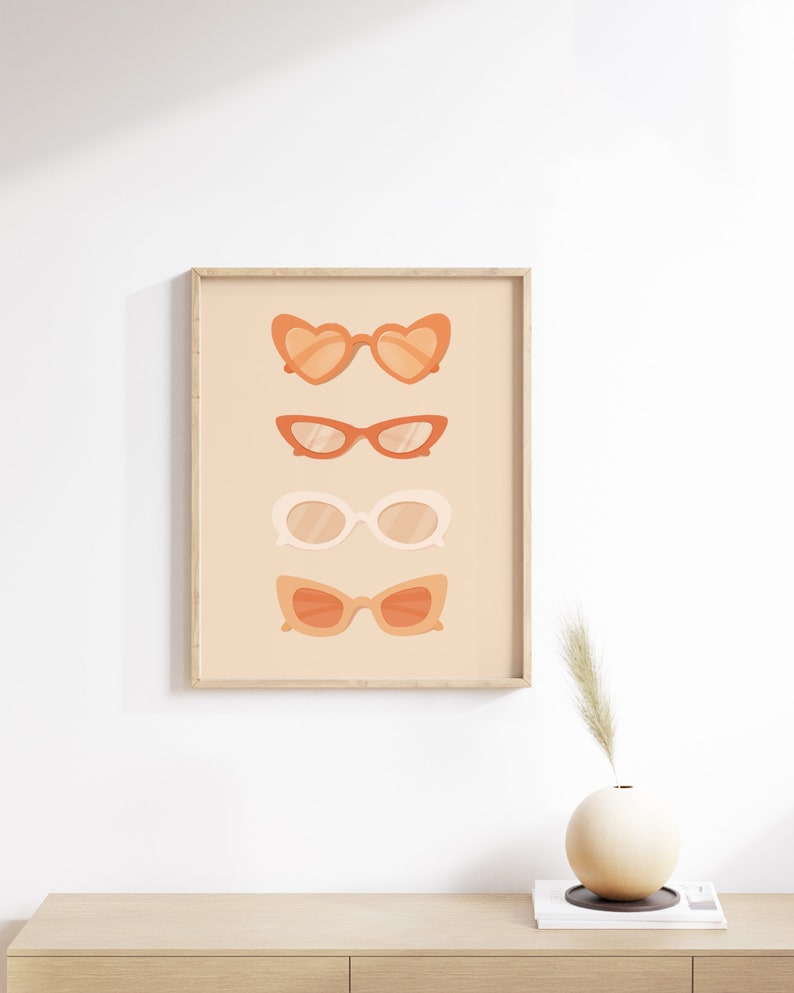 May include: A framed print with a peach background featuring four different styles of sunglasses in shades of orange and white.