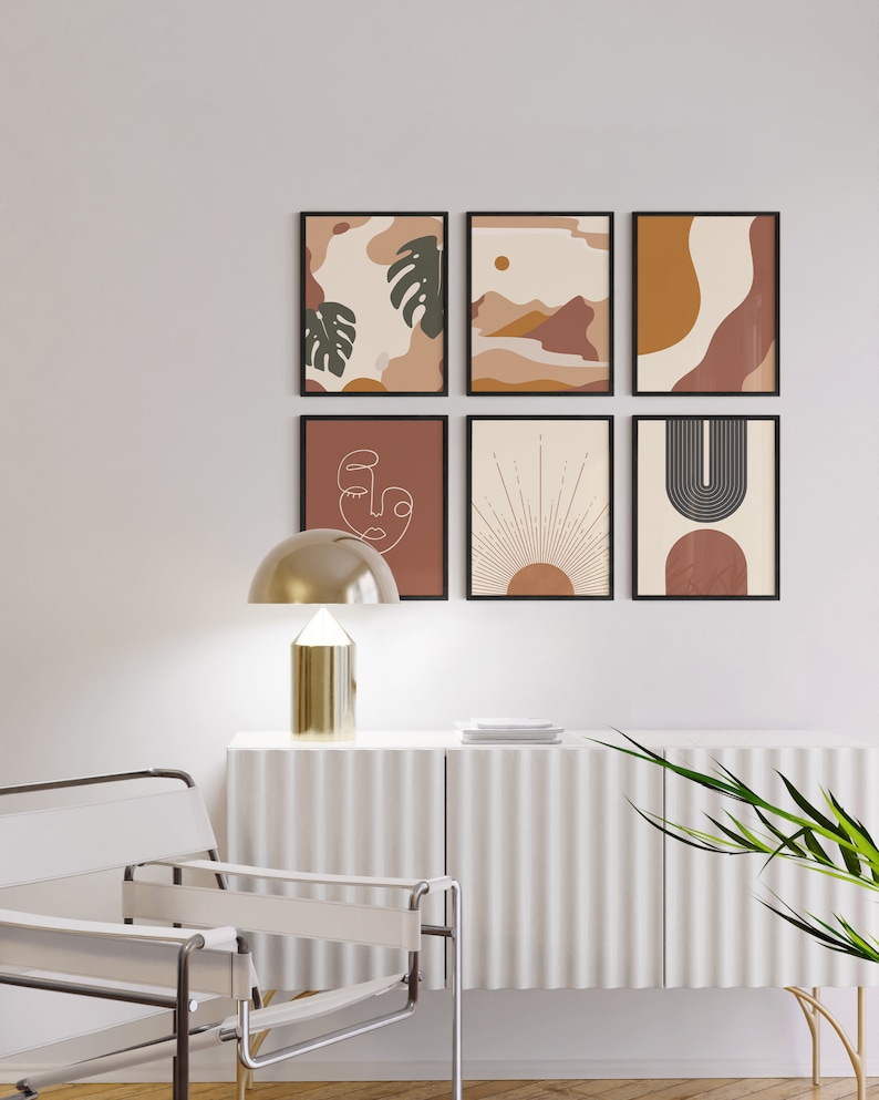 May include: A set of six framed abstract art prints in a minimalist style. The prints feature geometric shapes, line drawings, and organic forms in shades of brown, orange, and white. The prints are arranged in a grid pattern on a white wall.