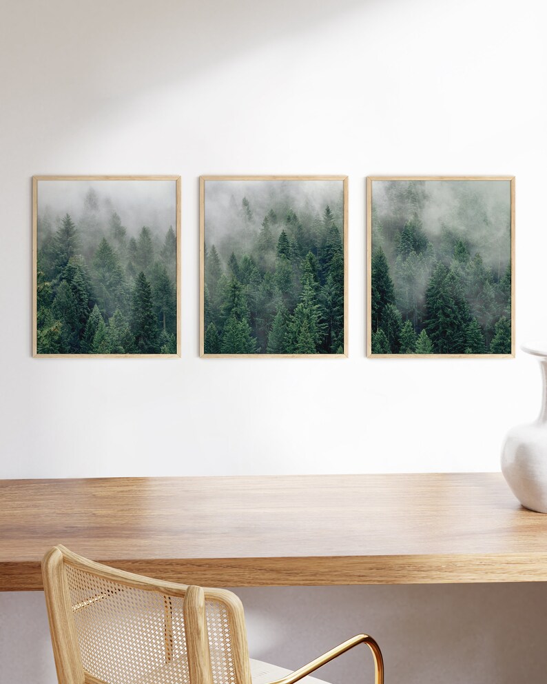 May include: Three framed prints of a misty forest with tall evergreen trees. The prints are arranged horizontally on a white wall above a wooden desk.