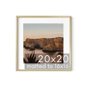 May include: A framed photograph of a rocky coastline with a blue ocean and a sunset sky. The frame is gold and the image is matted to 16x16 inches. The text "20x20 matted to 16x16" is printed below the image.