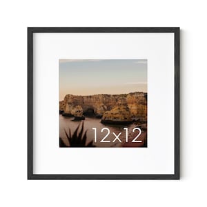 May include: A black framed photograph of a rocky coastline with a blue ocean and a sunset sky. The photo is 12 inches by 12 inches.