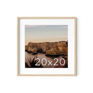 May include: A framed photograph of a rocky coastline with a sunset sky. The image is in a light wood frame with a white mat. The text "20x20" is printed in white on the image.