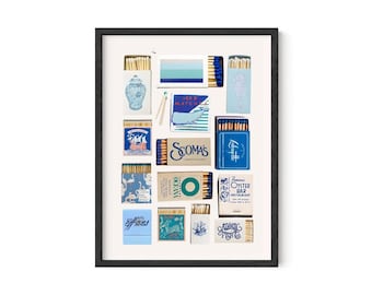 Op de afbeelding: Een ingelijste print met diverse lucifersdoosjes met nautische en kustmotieven. De lucifersdoosjes zijn in blauwe, witte en beige tinten, met illustraties van zeepaardjes, schepen en andere mariene elementen. De print zit in een zwarte lijst.