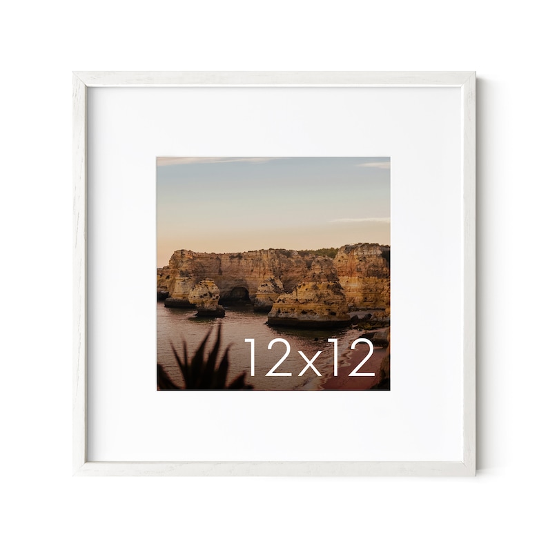Op de afbeelding: Een wit fotolijstje met een landschapsfoto van een rotsachtige kustlijn bij zonsondergang. De foto is in het midden onderaan met "12x12" gelabeld.