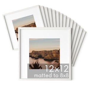 Op de afbeelding: Een set van 10 witte fotolijsten, elk met een afmeting van 30,5 x 30,5 cm, met een passe-partout voor een foto van 20,3 x 20,3 cm. De lijsten zijn in een waaier vorm gestapeld, met de bovenste lijst die een landschapsfoto van een rotsachtige kustlijn laat zien.