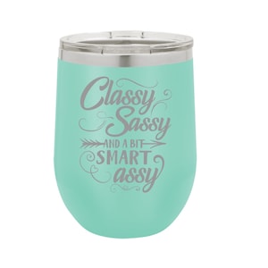 May include: A turquoise stainless steel wine tumbler with a silver lid. The tumbler has a white inscription that reads "Classy Sassy and a bit Smart Assy".
