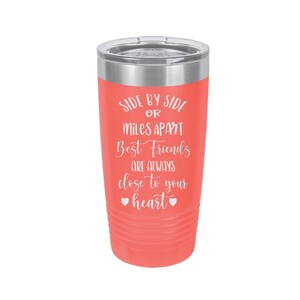 May include: Coral pink stainless steel tumbler with a white inscription that reads "Side by side or miles apart best friends are always close to your heart" with two small hearts at the bottom.