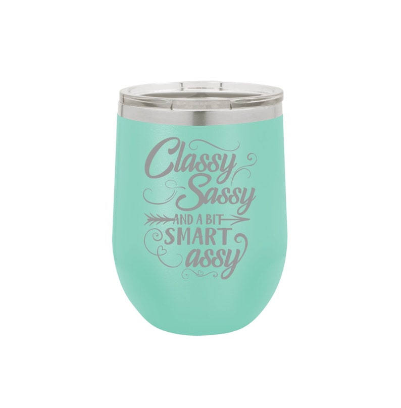 May include: A turquoise stainless steel wine tumbler with a silver lid. The tumbler has a white inscription that reads "Classy Sassy and a bit Smart Assy".