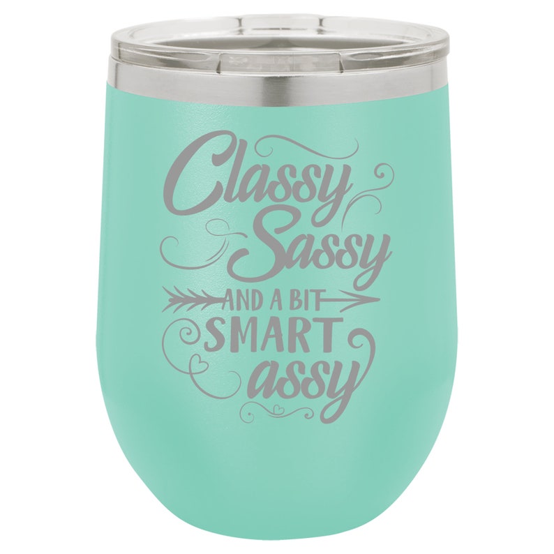 May include: A turquoise stainless steel wine tumbler with a silver lid. The tumbler has a gray inscription that reads "Classy Sassy and a bit Smart Assy".