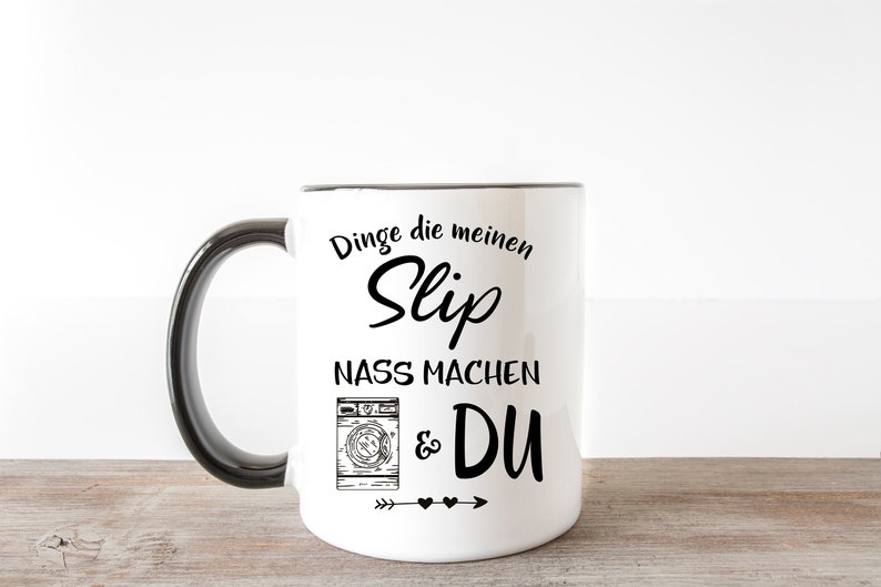 May include: White ceramic mug with a black handle. The mug has a black graphic that says "Dinge die meinen Slip nass machen & DU" with a drawing of a washing machine and arrows with hearts.