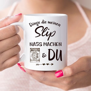 May include: White ceramic mug with black text that reads "Dinge die meinen Slip nass machen & DU" with a drawing of a washing machine and arrows with hearts.