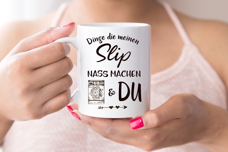May include: White ceramic mug with black text that reads "Dinge die meinen Slip nass machen & DU" with a drawing of a washing machine and arrows with hearts.