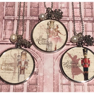 May include: Three silver necklaces with round glass pendants featuring a Nutcracker and ballerina theme. Each pendant has a white background with a vintage-style image of a Nutcracker and ballerina, and the text "Merry Christmas".