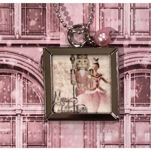 May include: A silver locket necklace with a pink pearl charm. The locket features a vintage image of the Nutcracker and a ballerina with the text "Merry Christmas".
