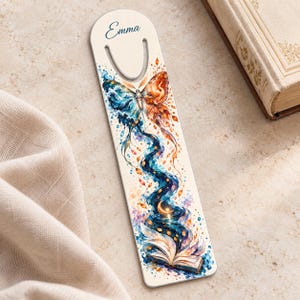 May include: A vertical bookmark with a rounded top and a cutout slot, featuring the name Emma in blue script. The design displays a butterfly with one blue wing and one orange wing, trailing into a swirling stream toward an open book.