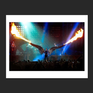 May include: A performer on stage wearing a black outfit with large, metallic wings that are shooting flames on either side. The performer is standing in front of a crowd of people.