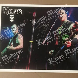 Puede incluir: Una fotografía en blanco y negro de dos músicos tocando en un escenario. Los músicos visten ropa negra y tocan guitarras eléctricas. El nombre de la banda "Misfits" está escrito en letras blancas sobre un fondo negro.