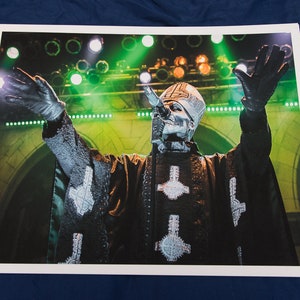 May include: A black and white photo of a person wearing a black and silver costume with a microphone in their hand. The person is standing on a stage with green and white lights in the background.