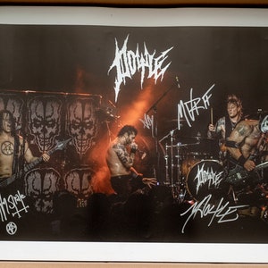 May include: A black and white photo of a rock band performing on stage. The band is called "1000000" and the photo is signed by the band members. The band members are wearing black clothing and are playing instruments. The stage is lit with red and orange lights.