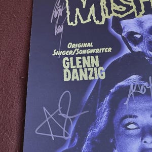 May include: A dark blue poster featuring the band "The Misfits" with the text "Original Singer/Songwriter Glenn Danzig". The poster has multiple signatures in white ink and a stylized image of a person.